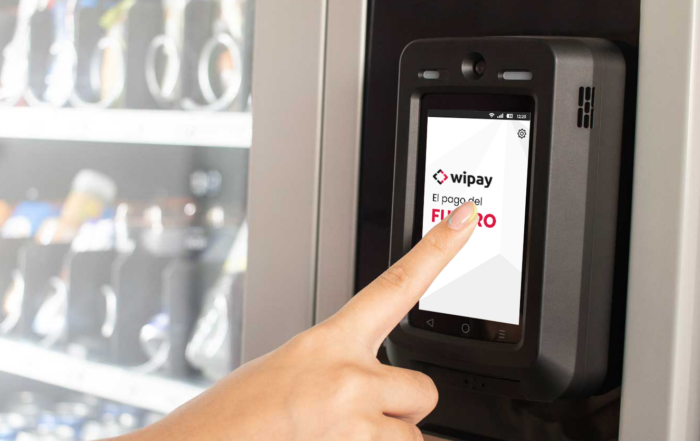 La imagen muestra un dispositivo de pago con tarjeta instalado en una maquina expendedora y un usuario operando con el mismo